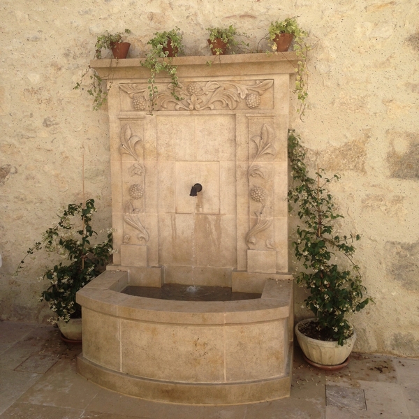 fontaine adossée en pierre avec margelle et fronton mural sculpté de motifs végétaux