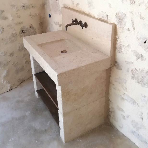 vasque de salle de bain en pierre naturelle calcaire taillée sur mesure avec une cuve peu profonde et une crédence, le tout sur des jambages en pierre