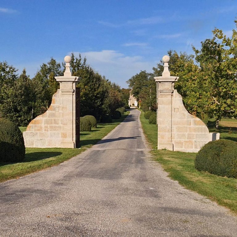 paire de piliers de portail en pierre naturelle avec moulures et boules en pierre le tout réalisé en France sur mesure avec une grille en fer forgé