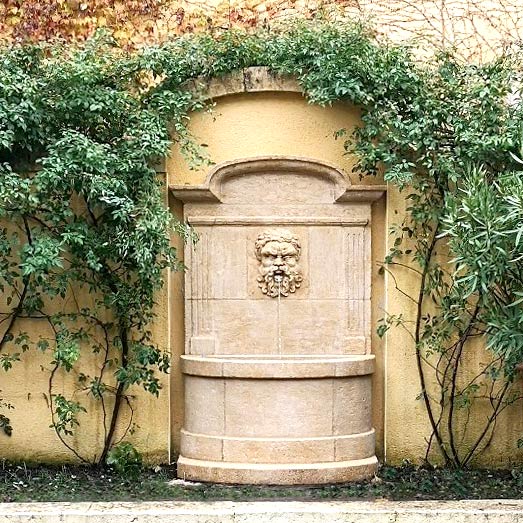 fontaine de jardin murale adossée au mur avec un bassin cintré et un fronton avec corniche en chapeau de gendarme et mascaron sculpté sculpture visage homme barbu bacchus dionysos neptune